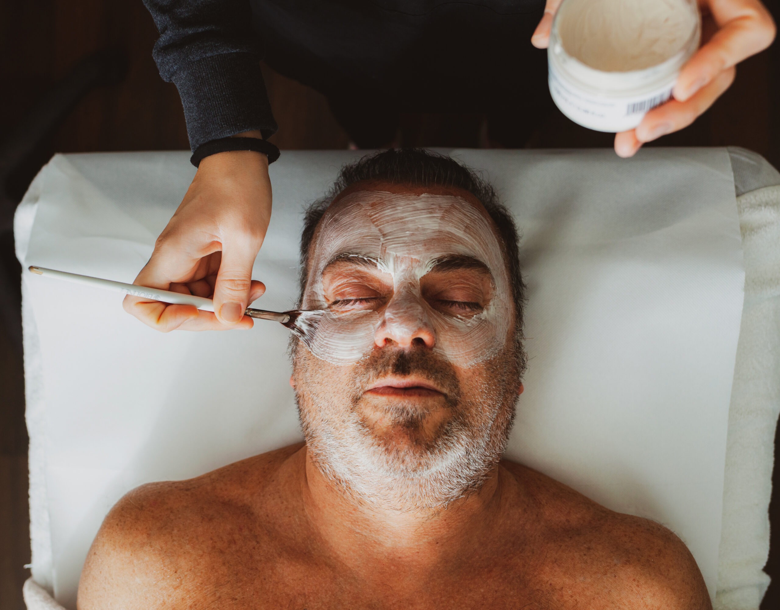 Ein Mann mittleren Alters in einem Schönheitssalon mit einer Gesichtsmaske.